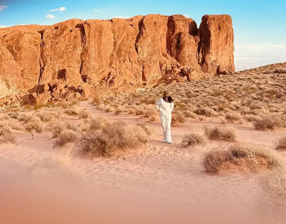 Walker on a sandy trail beneath a tall red sandstone wall on a Valley of Fire hike, Nevada